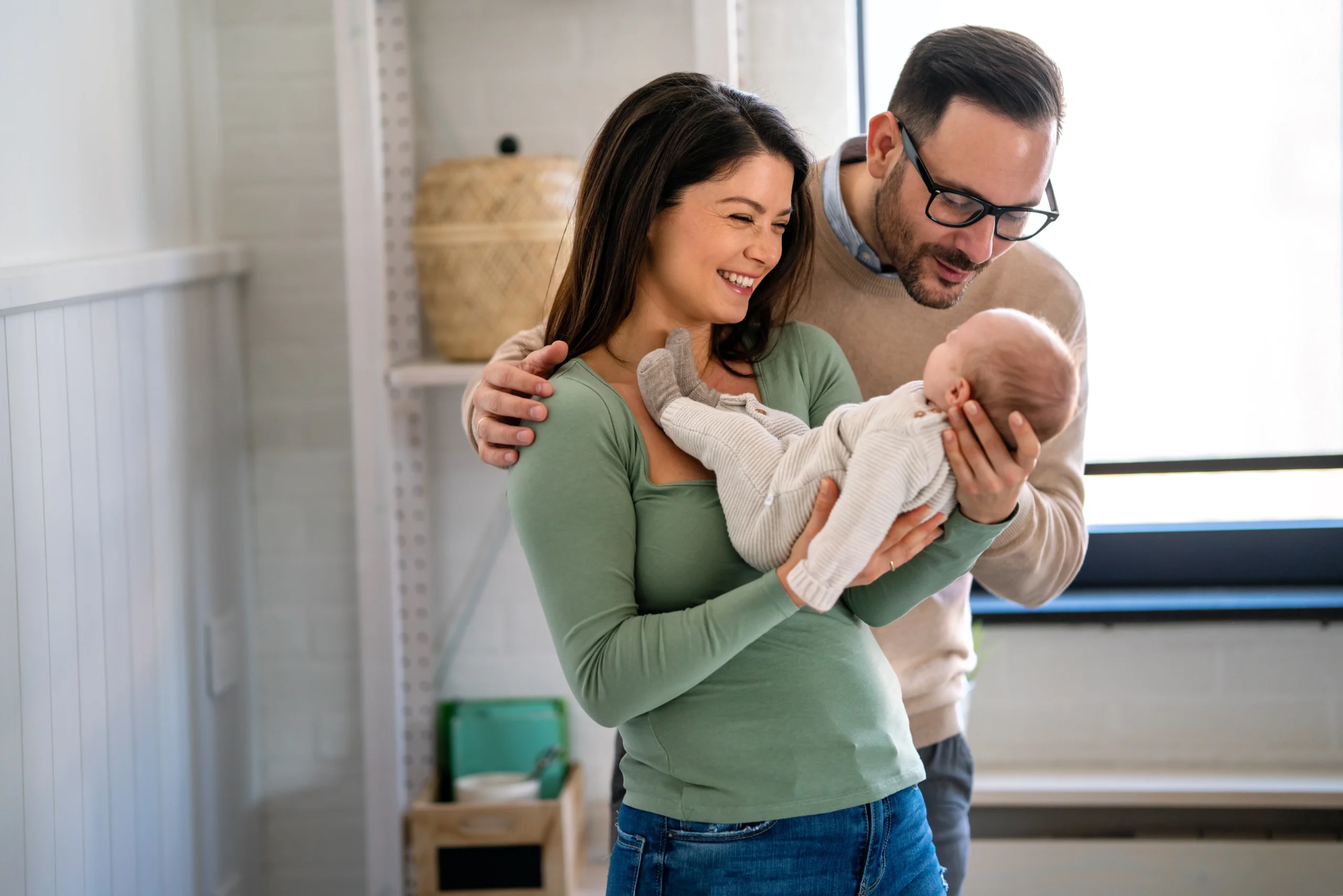 A man and woman stand next to each other smiling and holding a newborn baby.