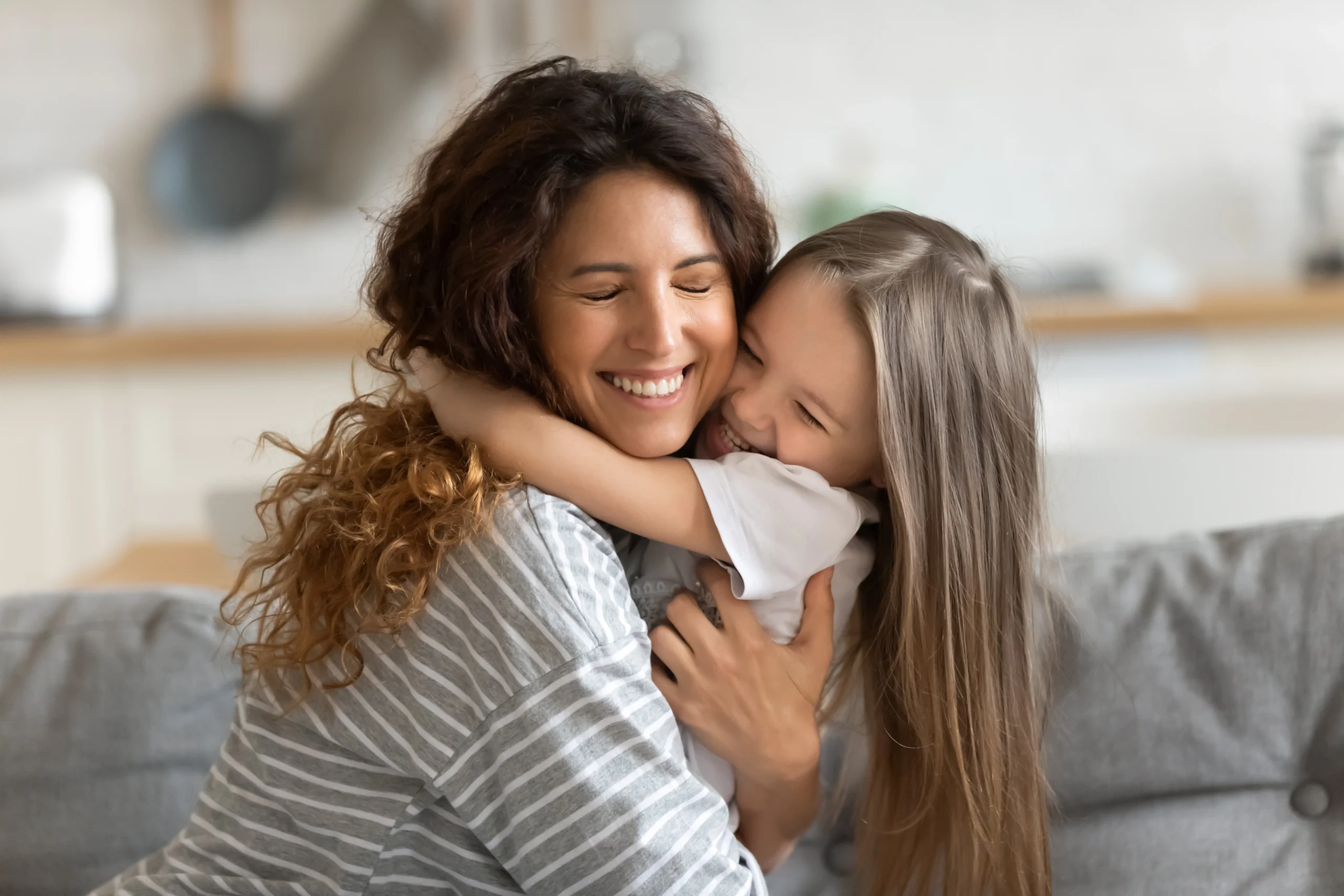 A woman embraces her daughter in a big hug on a couch
