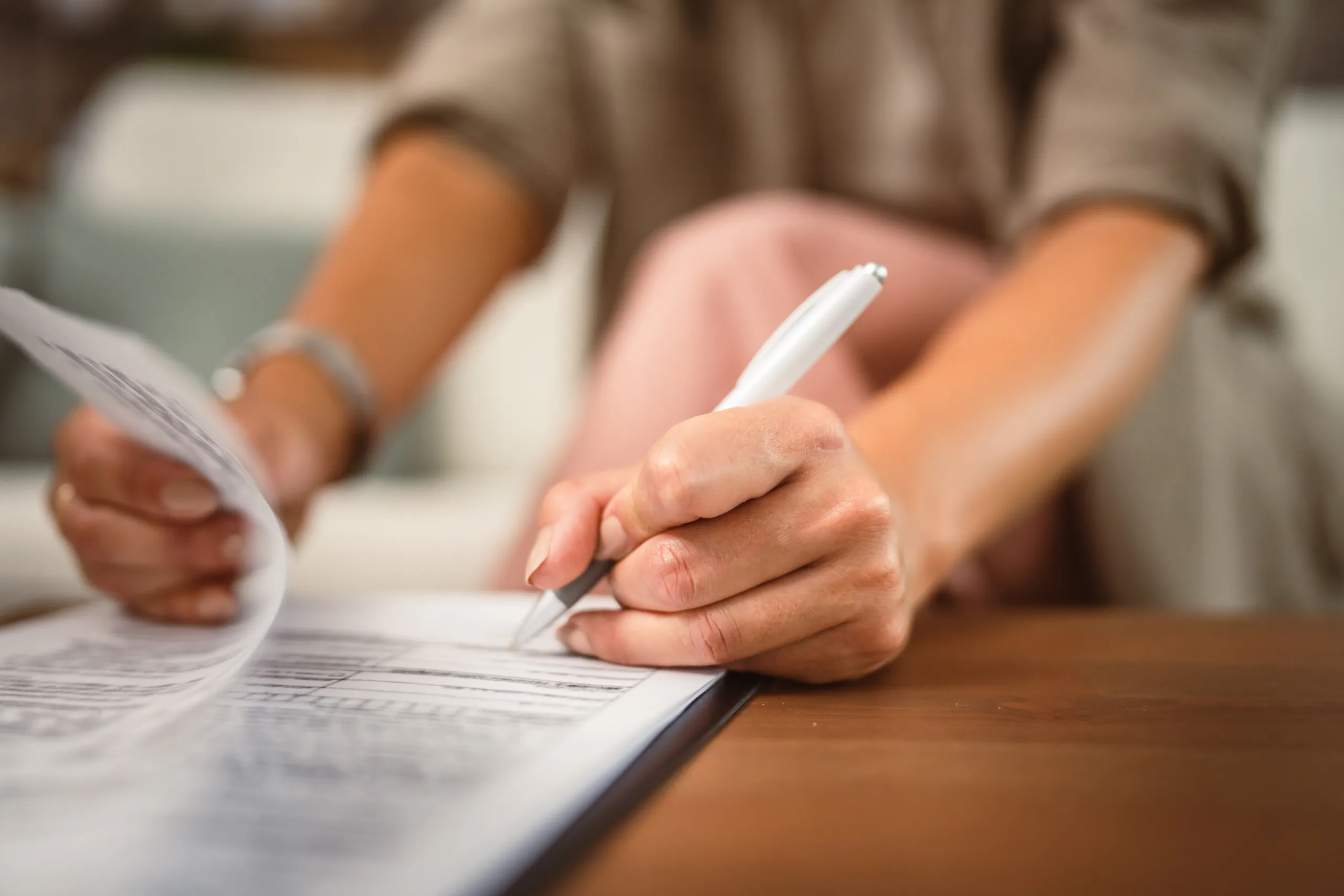 A woman signs papers on a clipboard on a table.