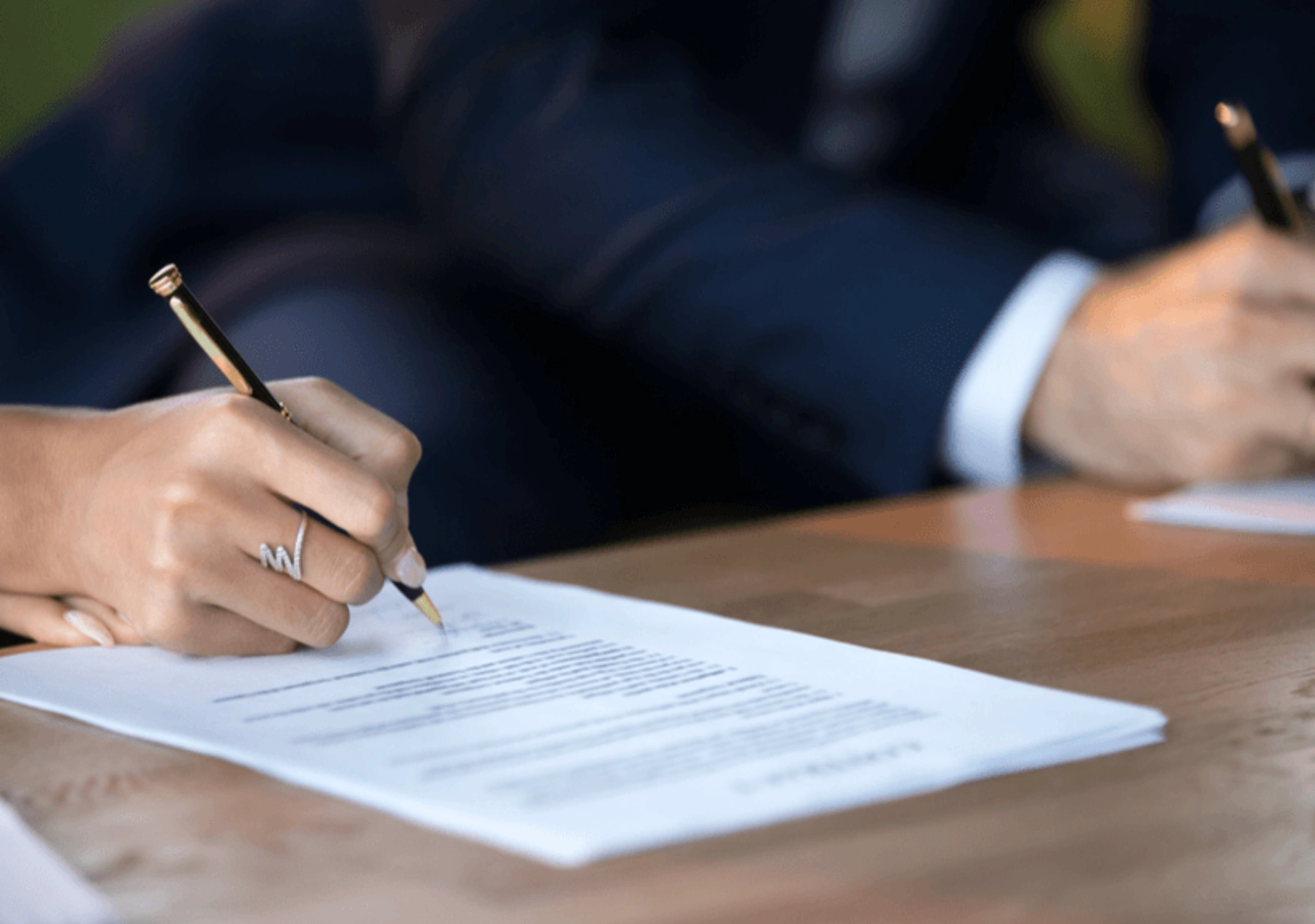 A woman and man sit next to each other signing forms on a table.